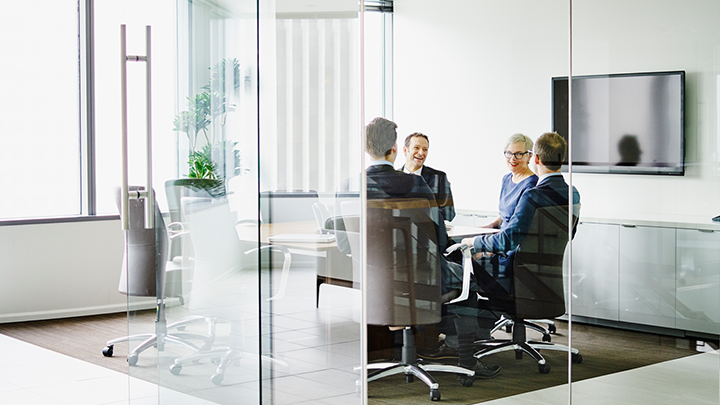 Four people in a glass-walled conference room