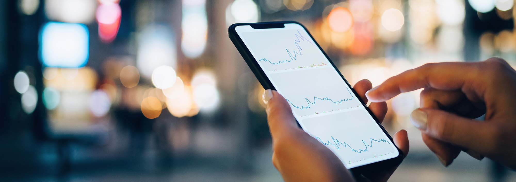 Closeup of someone holding a cellphone with city lights in the background