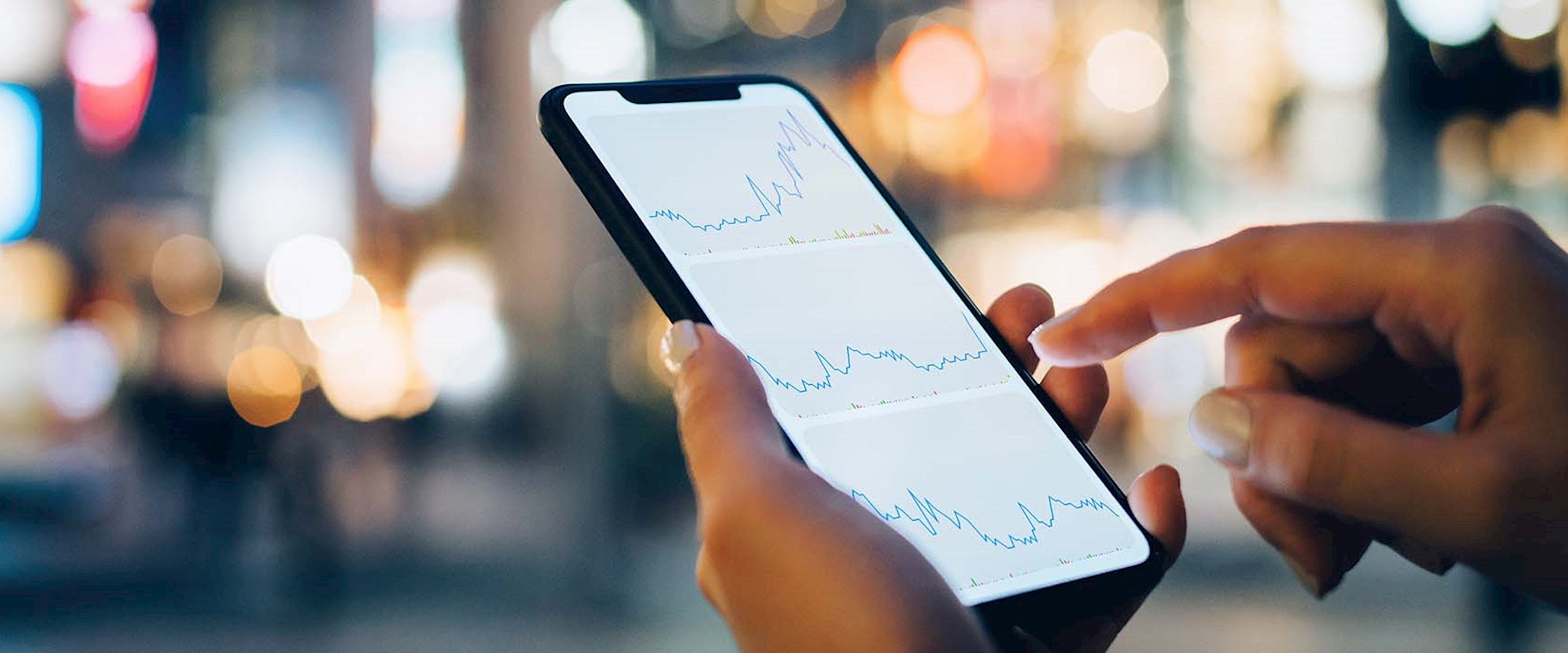 Closeup of someone holding a cellphone with city lights in the background