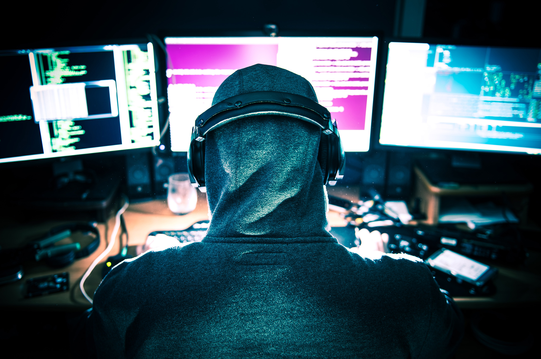 Person in hood in front of computer screens