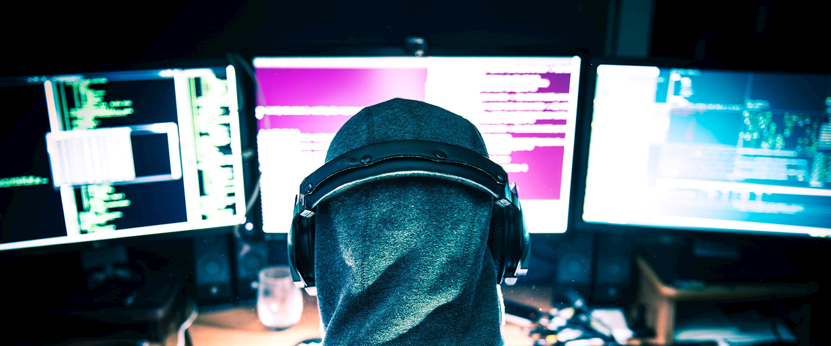 Person in hood in front of computer screens