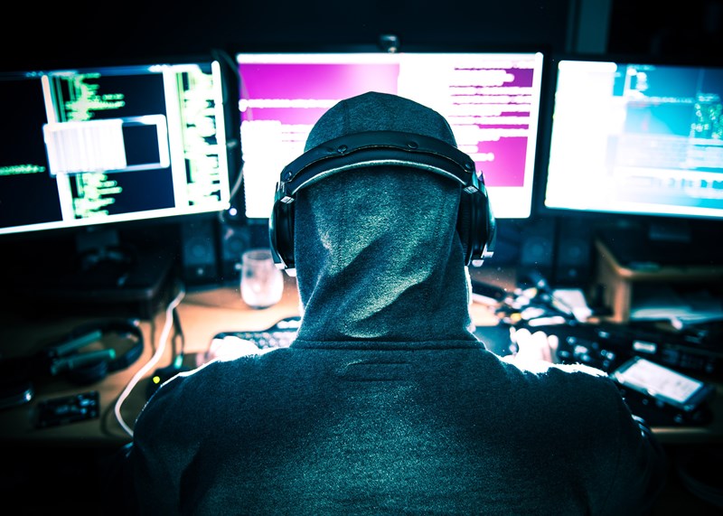 Person in hood in front of computer screens