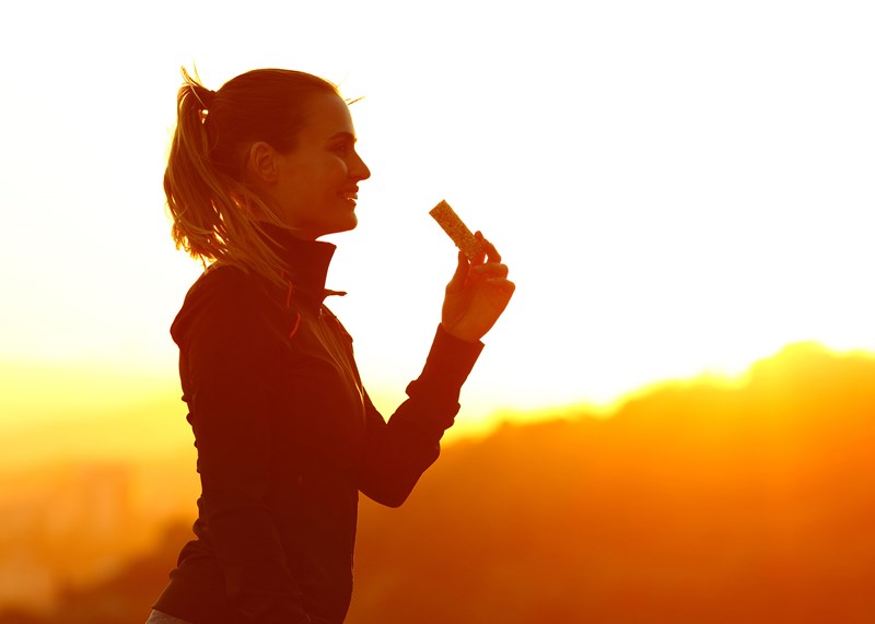 Woman eating a granola bar at sunset