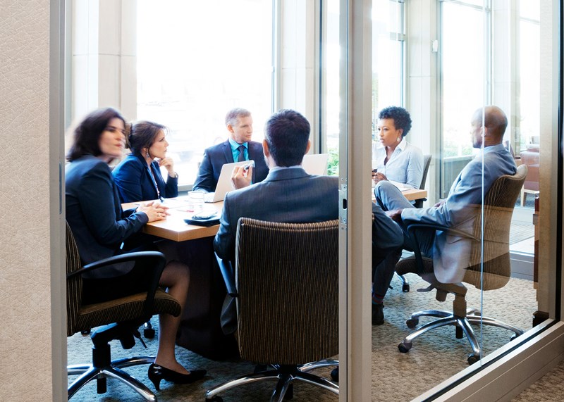 a small group of men and women in a meeting room with glass windows