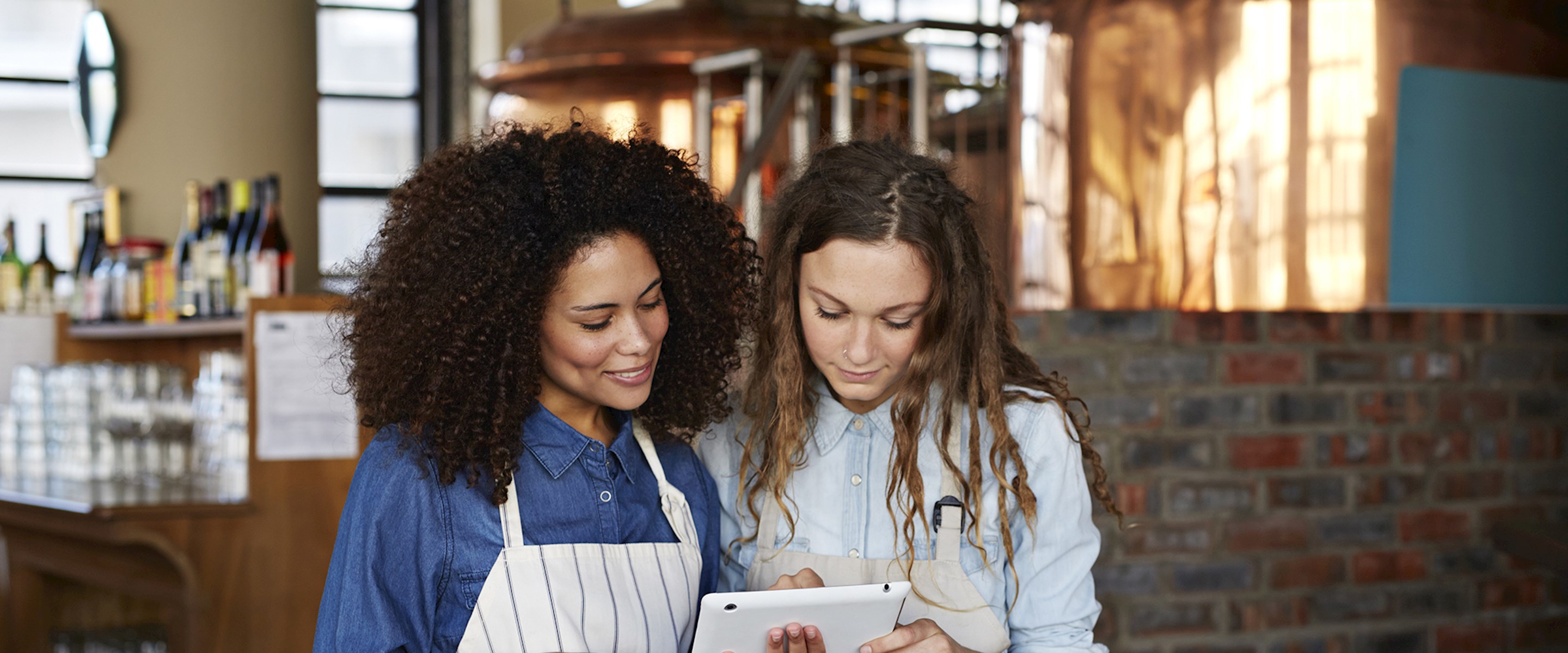 Two women in aprons looking at a tablet