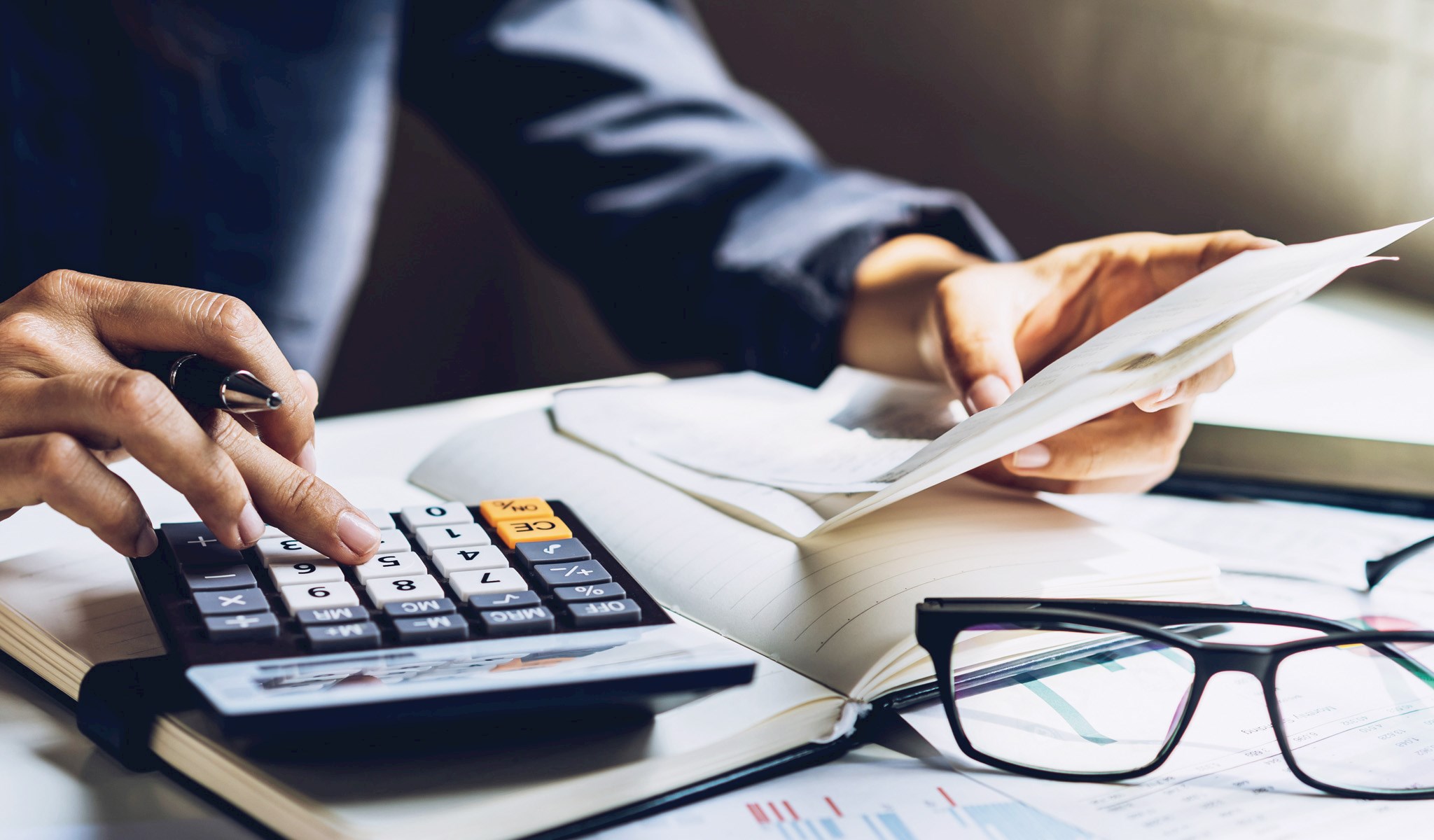 Hand on a calculator on a desk with papers