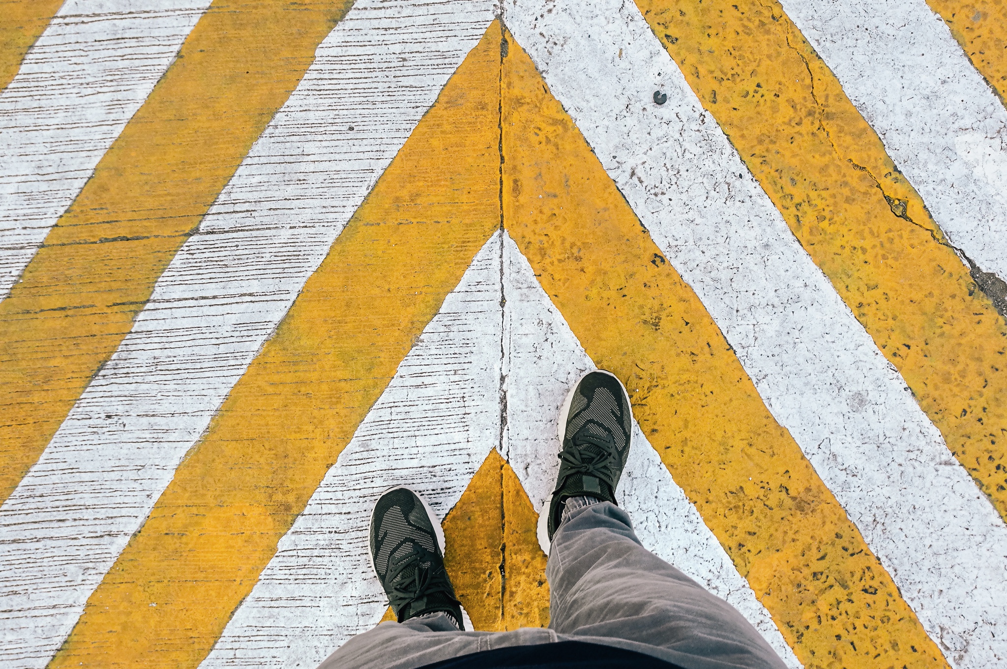 Looking down at feet on a yellow and white crosswalk